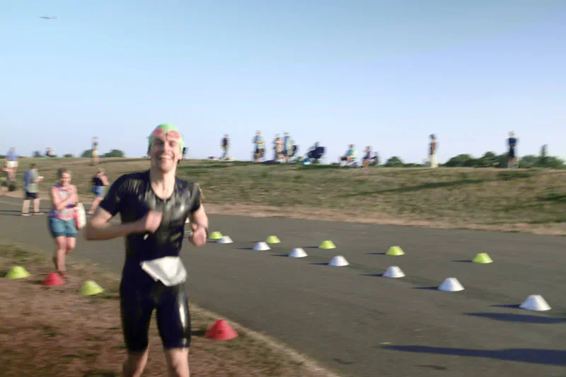 Running out of the swim in a wetsuit and green swim cap